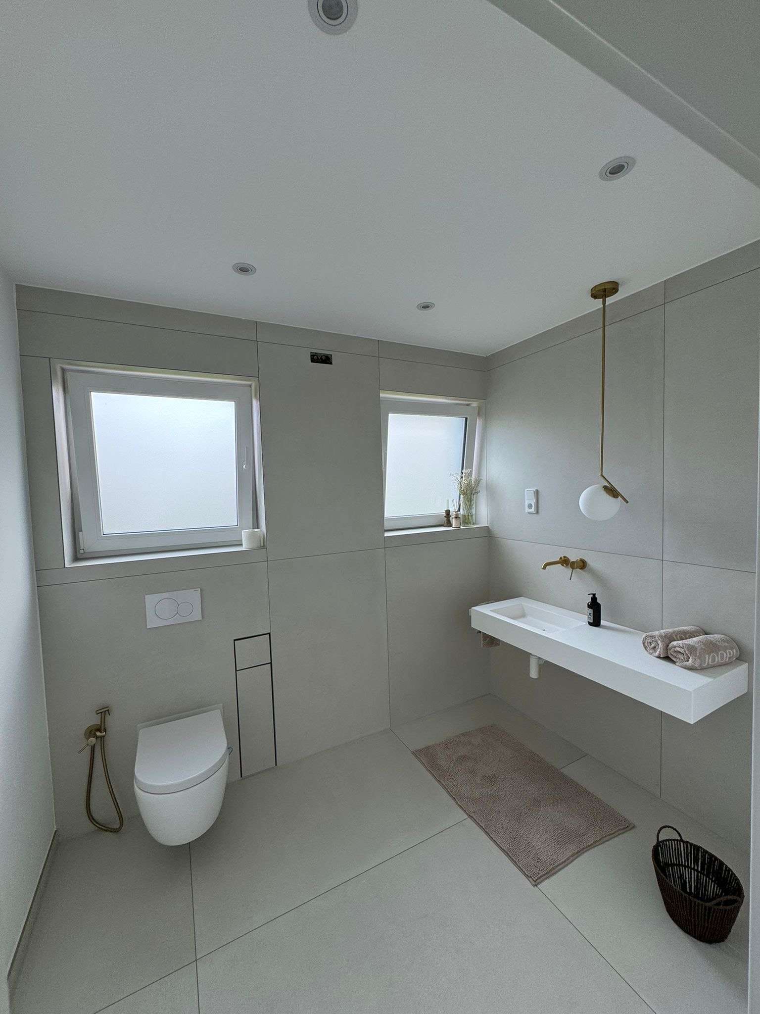 Badezimmer mit XXL-Feinsteinzeug in Betonoptik greige, wandhängendes WC und goldene Armaturen