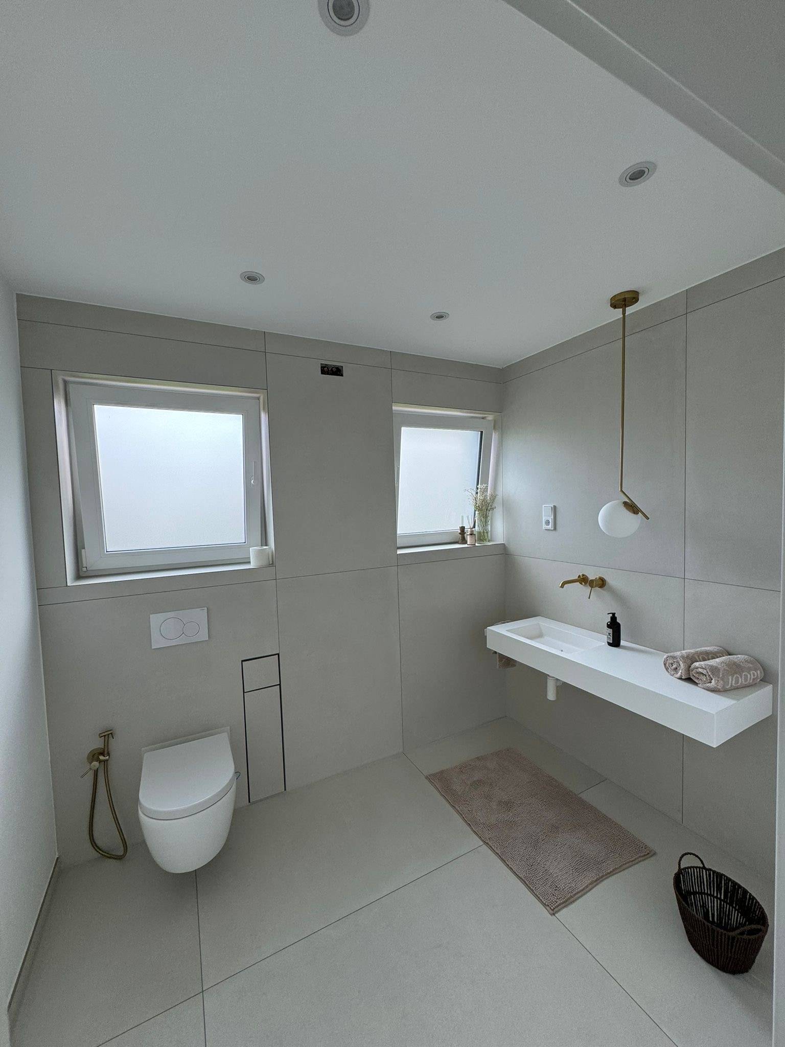 Badezimmer mit XXL-Feinsteinzeug in Betonoptik greige, wandhängendes WC und goldene Armaturen