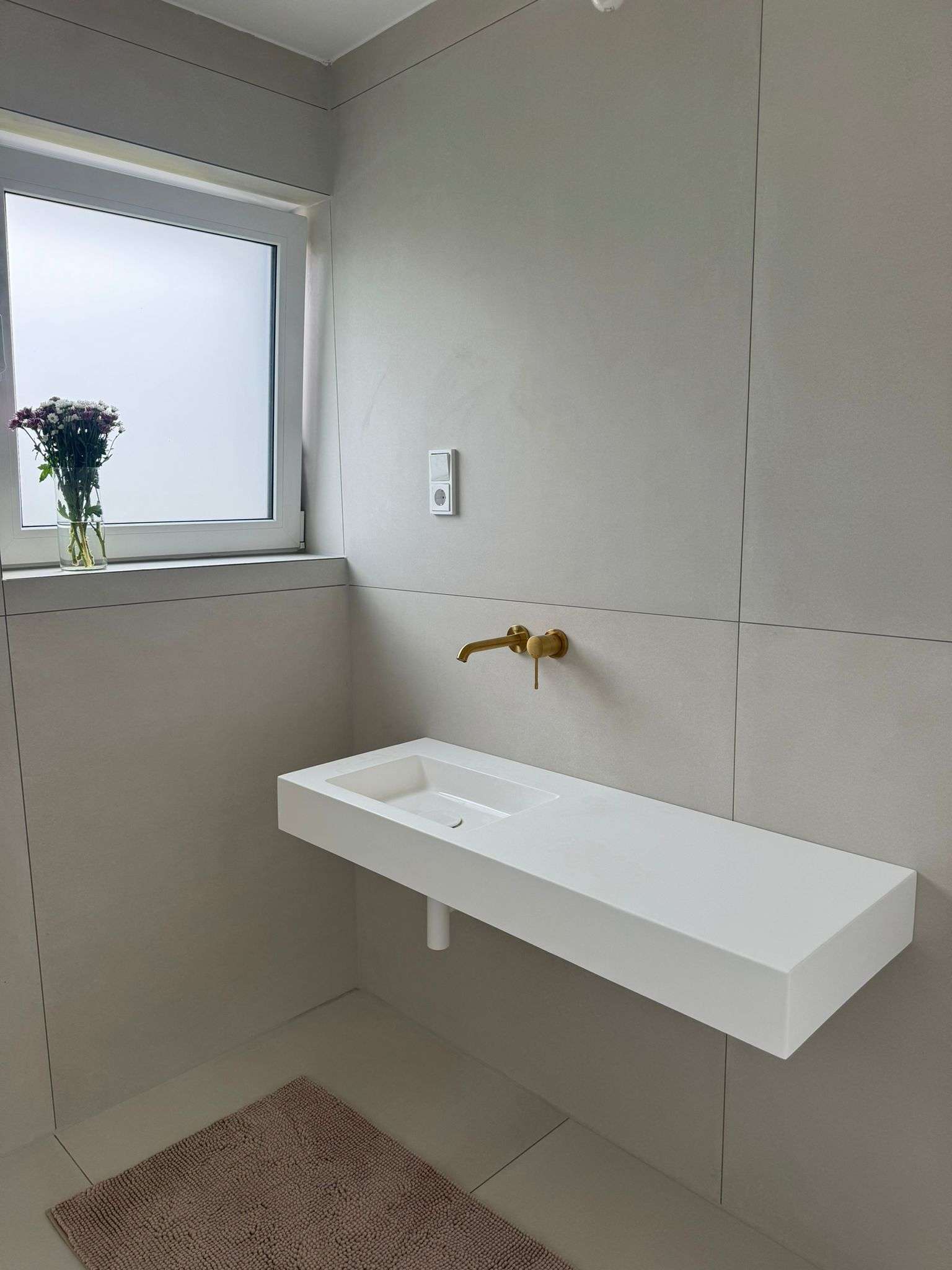 Waschtischbereich mit cremefarbenem XXL-Feinsteinzeug, wandmontiertem Waschtisch und goldener Wandarmatur